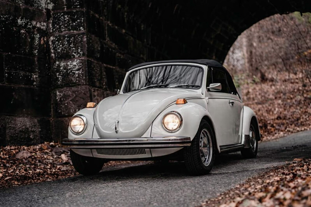 Classic white Volkswagen Super Beetle convertible under stone bridge representing 19711979 model years