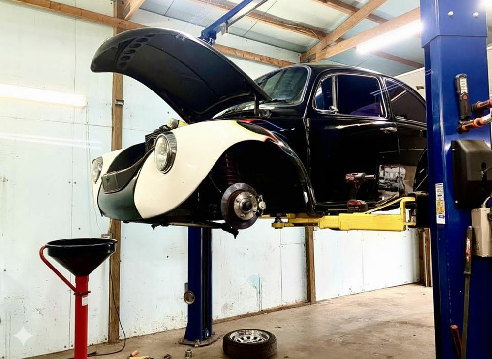 A classic Volkswagen Super Beetle on a lift in a professional garage setting, ready for an engine oil change.